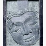 A hand-carved stone relief plaque of a serene Buddha face with closed eyes, set within a rustic dark metal frame, perfect for zen wall decor and meditation rooms.