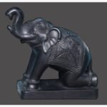 A polished black stone elephant sculpture with its trunk raised, featuring traditional carved blankets and ornaments, mounted on a solid rectangular base.