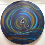 Circular abstract acrylic painting titled Swirl of Nature by Mansi Virani featuring swirling blue, teal, and gold vortex lines surrounding patterned black-and-white stylized flowers and birds.